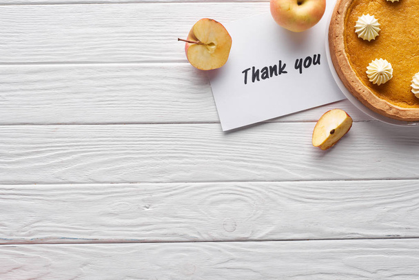 top view of pumpkin pie, ripe apples and thank you card on wooden white table - 写真・画像
