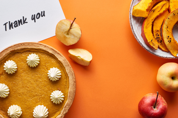 top view of pumpkin pie, ripe apples and thank you card on orange background - 写真・画像