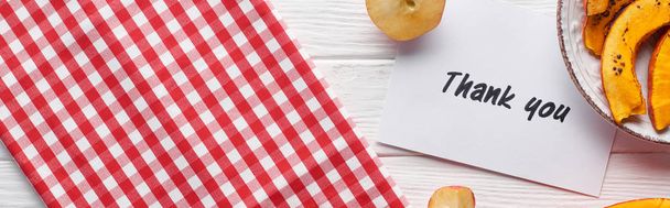 Κορυφαία θέα της κολοκύθας, ώριμα μήλα και ευχαριστήρια κάρτα σε ξύλινο λευκό τραπέζι με καρό πετσέτα, πανοραμική βολή - Φωτογραφία, εικόνα