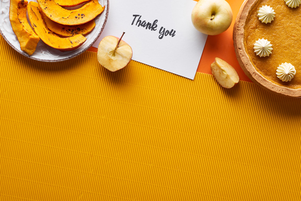 top view of pumpkin pie, ripe apples and thank you card on orange background with copy space - Photo, Image
