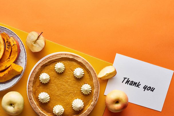 top view of pumpkin pie, ripe apples and thank you card on orange background - 写真・画像