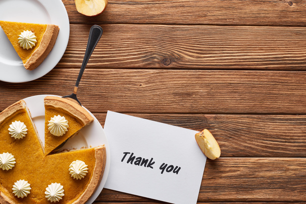 Ansicht von Kürbiskuchen, reifen Äpfeln und Dankeskarte auf einem hölzernen braunen Tisch - Foto, Bild