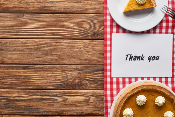 Draufsicht auf Kürbiskuchen und Dankeskarte auf hölzernem braunem Tisch mit rot karierter Serviette - Foto, Bild