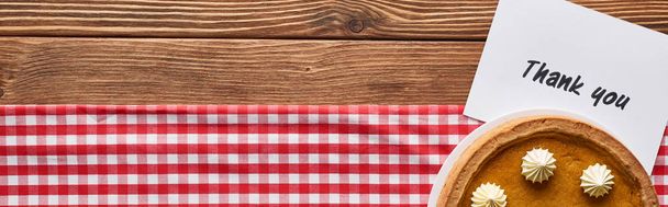 top view of pumpkin pie and thank you card on wooden brown table with red plaid napkin, panoramic shot - Foto, Bild