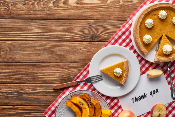 top view of pumpkin pie, ripe apples and thank you card on wooden brown table with red plaid napkin - Photo, Image
