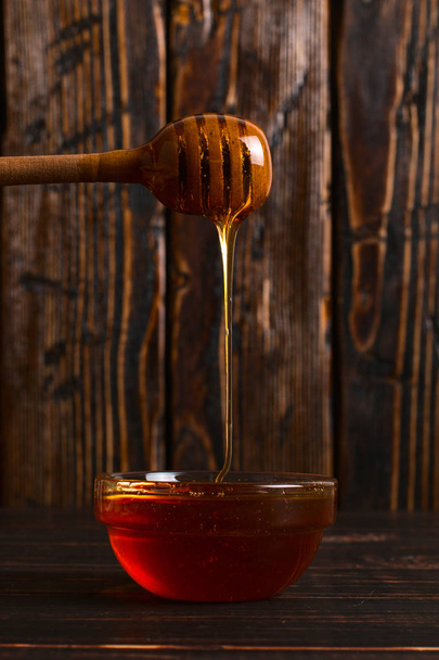 Honey flows from a stick into a jar. Rustic sweet photo, wooden  - Zdjęcie, obraz