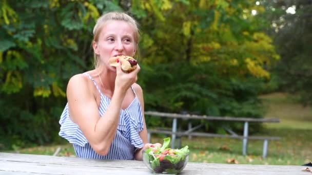 Γυναίκα που τρώει χοτ ντογκ καθισμένος σε εξωτερικούς χώρους. - Πλάνα, βίντεο