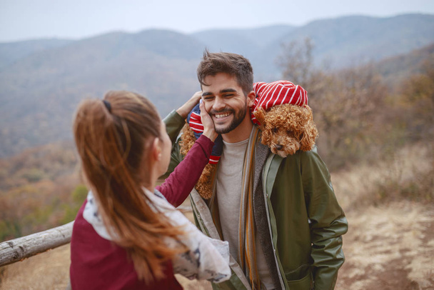 Woman flirting with her mixed race boyfriend while standing in nature at autumn. Man holding their dog on shoulders. - Photo, Image