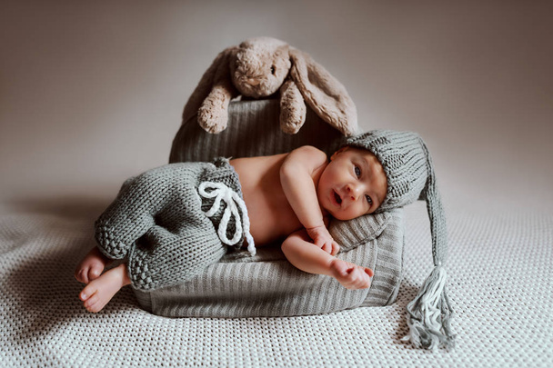 Повна довжина чарівного новонародженого хлопчика, одягненого в трикотажні штани і з в'язаною шапочкою на голові лежить в маленькому кріслі
. - Фото, зображення
