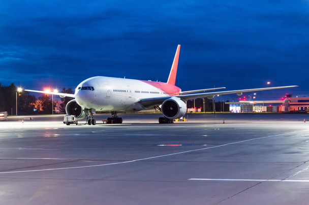 Vista nocturna del aeropuerto y un gran avión de pasajeros en el estacionamiento antes del vuelo
. - Foto, Imagen