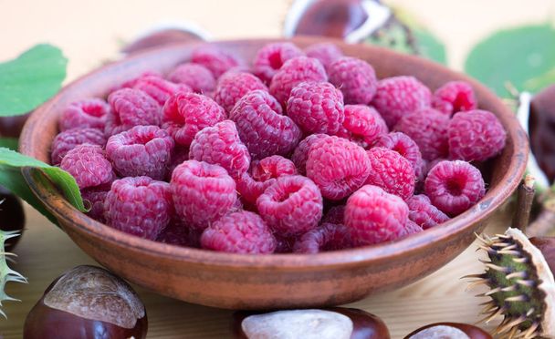 Fresh raspberries background closeup photo. Red raspberries in ceramic bowl on wooden table, chestnuts.  - Photo, Image
