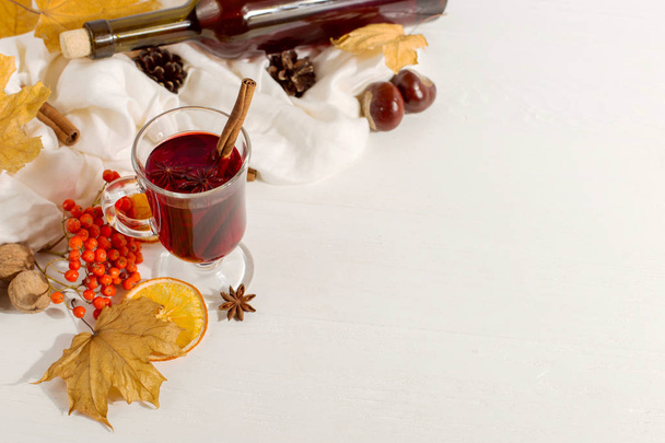 A cup of mulled wine with spices, bottle, scarf, spices, dry leaves and oranges on the table. Autumn mood, method to keep warm in cold, copy space. - Foto, Bild