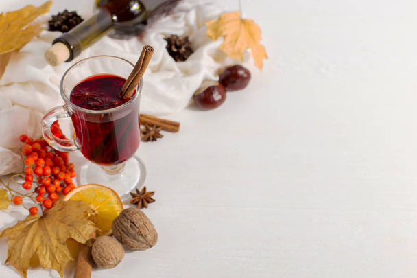A cup of mulled wine with spices, bottle, scarf, spices, dry leaves and oranges on the table. Autumn mood, method to keep warm in cold, copy space. - Foto, Bild