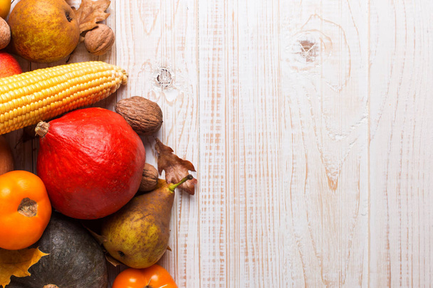 Different vegetables pumpkins, apples, pears, nuts, corn, tomatoes, dry yellow leaves on white wooden background. Autumn Harvest concept, copy space. - 写真・画像