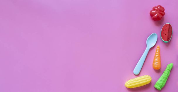 Säuglingsnahrung. mit Baby-Accessoires und Spielzeug auf rosa Hintergrund. Gesunde Ernährung. Obst und Gemüse. Kopierraum. - Foto, Bild
