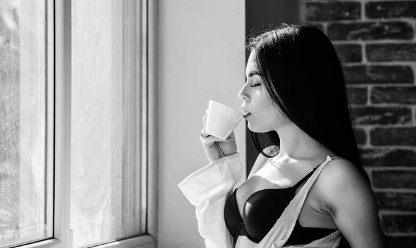 Best thing to drink in the morning. Adorable girl holding cup with tasty coffee drink. Sexy woman enjoying her drink recipe. Pretty woman drinking healthy morning drink at window - Fotó, kép
