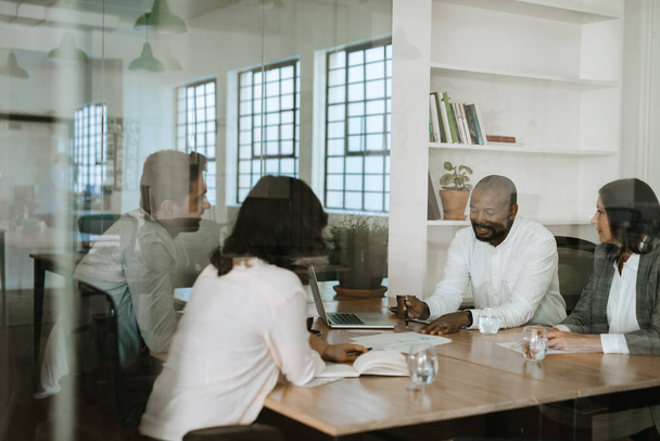 Group of diverse businesspeople talking together during a meeting around a table inside of a glass office boardroom - Foto, Imagem