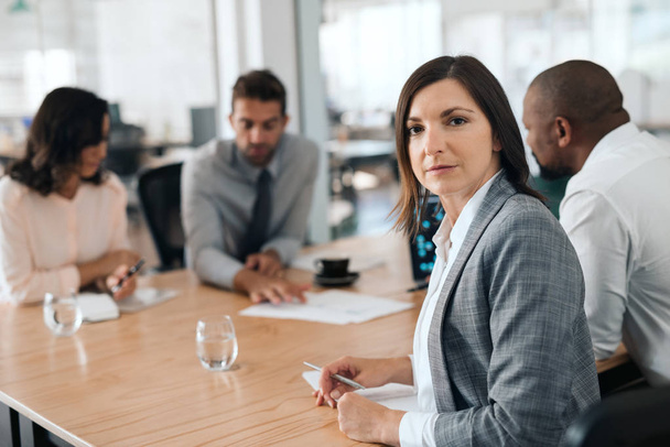 Portrait of a focused businesswoman sitting with a diverse group of colleagues at a boardroom table during a meeting in an office - Foto, Bild