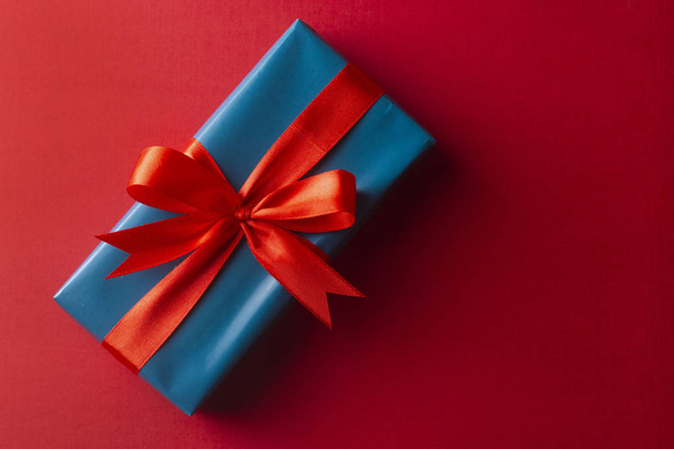 Blue gift box with red ribbon and bow isolated on red background, top view. Christms, party concept. - Foto, afbeelding