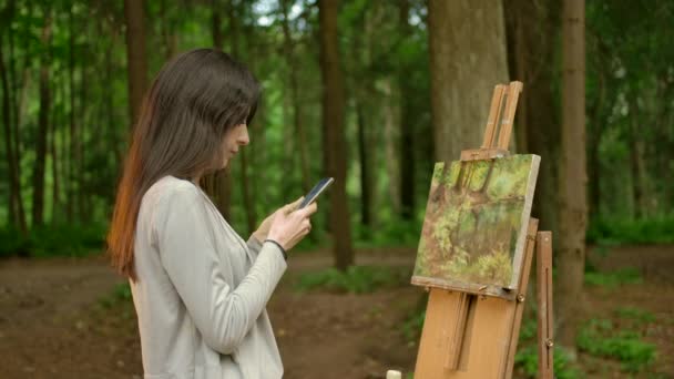 Το κορίτσι καλλιτέχνης ολοκλήρωσε την εργασία για τη ζωγραφική της και συνομιλούν στο smartphone της - Πλάνα, βίντεο