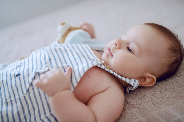 Close up of adorable baby boy lying on bed and waiting for his mother to pick him up. - Photo, Image