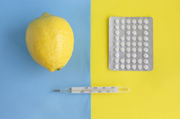 Fresh lemon, pack of tablets and thermometer on blue yellow background. Minimal style in season of common cold and flu virus, choice of treatment. Flat lay, top view. - Fotó, kép