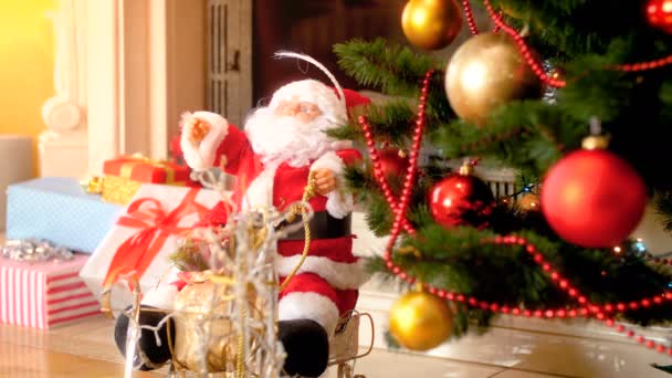 Κοντινό πλάνο 4K της κούκλας του Άη Βασίλη κάτω από το διακοσμημένο χριστουγεννιάτικο δέντρο δίπλα στο τζάκι στο σαλόνι. Τέλεια βολή για χειμερινές γιορτές και διακοπές - Πλάνα, βίντεο