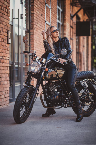 Handsome female biker is posing for photographer with her motorbike - Foto, Bild