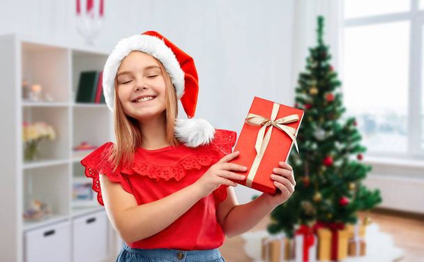 girl in santa hat with christmas gift at home - Foto, afbeelding