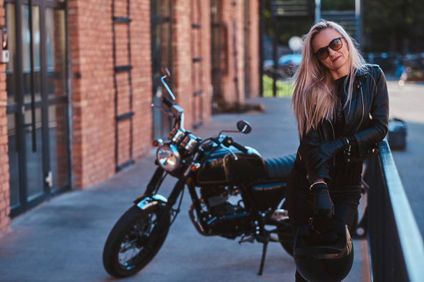 ハンサムな女性バイカーは彼女のバイクで写真家のためにポーズをとっています - 写真・画像