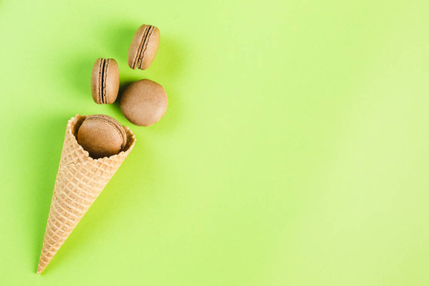 Шоколадні макаруни у вафельному конусі на зеленому тлі, зверху
  - Фото, зображення