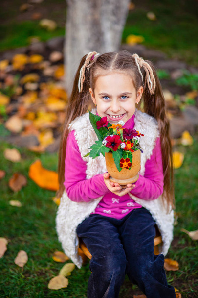 Cute happy girl with autumn bouquet of flowers in the garden on a sunny autumn day. - Фото, зображення