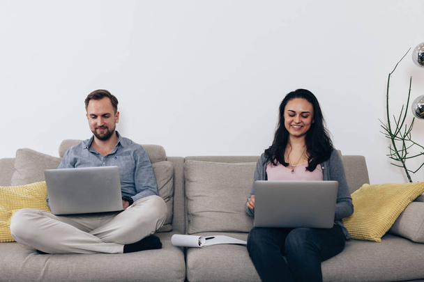 una feliz pareja de trabajo con el ordenador portátil en casa sentado en el sofá
 - Foto, imagen