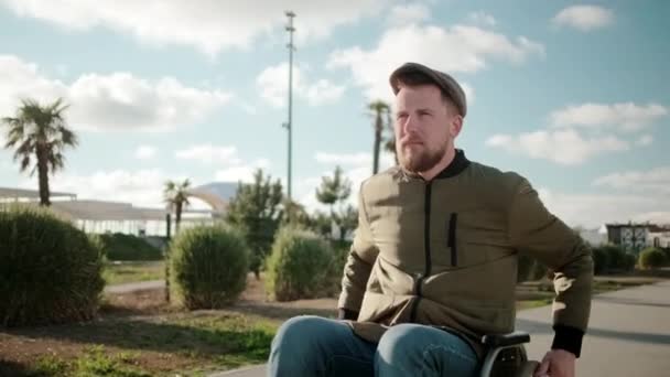 Homem barbudo confiante está montando em cadeira de rodas ao ar livre sozinho em dia ensolarado
 - Filmagem, Vídeo