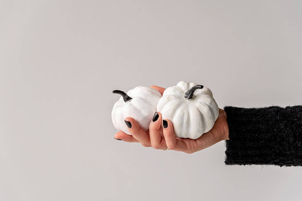 Mão feminina com unhas pretas segurando abóboras brancas e pretas halloween
 - Foto, Imagem