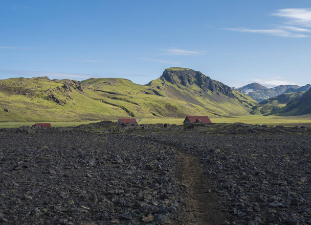 Hvanngil campsite path in lava field and green valley, small houses of hvanngil hut. volcanic mountains volcanic landscape with blue sky, Laugavegur Trail between Emstrur-Botnar and Alftavatn, central - Photo, Image