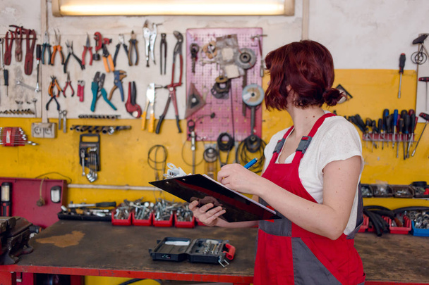 Χαριτωμένο, γυναίκα μηχανικός σε κόκκινο δουλειά φορούν φόρμες γράφει στο Πρόχειρο - Φωτογραφία, εικόνα