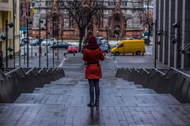 outono chuvoso tempo frio nublado e menina no casaco ficar de volta para a câmera em escadas de concreto cinza no beco da rua traseira da capital ucraniana Kiev
  - Foto, Imagem