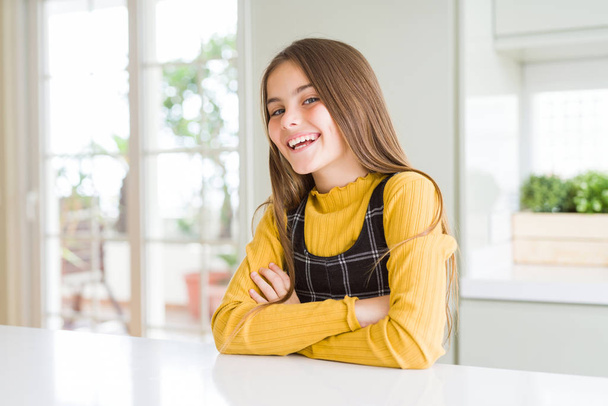 Jonge mooie blonde meisje draagt casual gele trui thuis gelukkig gezicht glimlachend met gekruiste armen kijken naar de camera. Positief persoon. - Foto, afbeelding