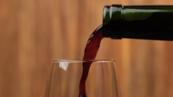 Close-up of red wine pouring in wine glass at wooden background. Slow motion of pouring red wine from bottle into goblet. Macro shot - Πλάνα, βίντεο