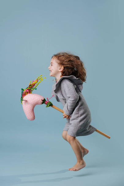 Little girl is hopping on a hobbyhorse, hovering in the air over blue background - Foto, Bild