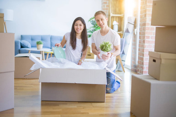 Молодая красивая пара стоит на полу держа доску с сообщением в новом доме вокруг картонных коробок
 - Фото, изображение