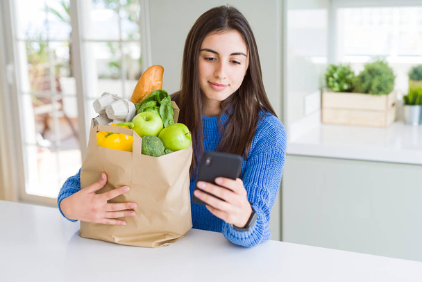 Mujer joven sosteniendo una bolsa de papel llena de alimentos frescos y usin
 - Foto, imagen