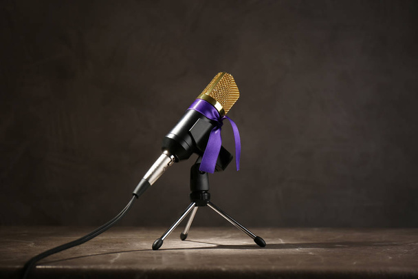 Microphone with purple awareness ribbon on wooden table against dark background - Φωτογραφία, εικόνα
