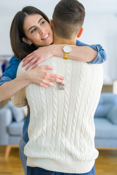 Young couple moving to a new home, hugging in love showing keys of new apartment smiling very happy - Foto, afbeelding