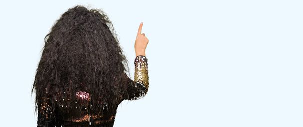Young beautiful girl with curly hair wearing night party dress Posing backwards pointing behind with finger hand - Photo, Image