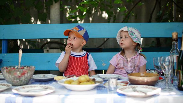 Vicces óvodáskorú gyermek ül egy asztalnál együtt, és várja az ebédet. - Fotó, kép
