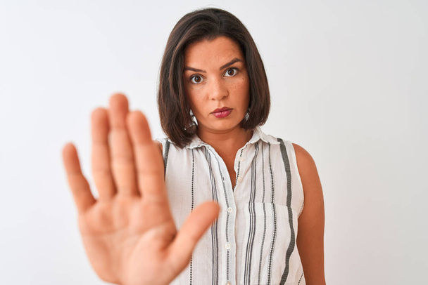 Молодая красивая женщина в повседневной полосатой рубашке стоя на изолированном белом фоне с открытой рукой делает знак стоп с серьезным и уверенным выражением лица, защитный жест
 - Фото, изображение