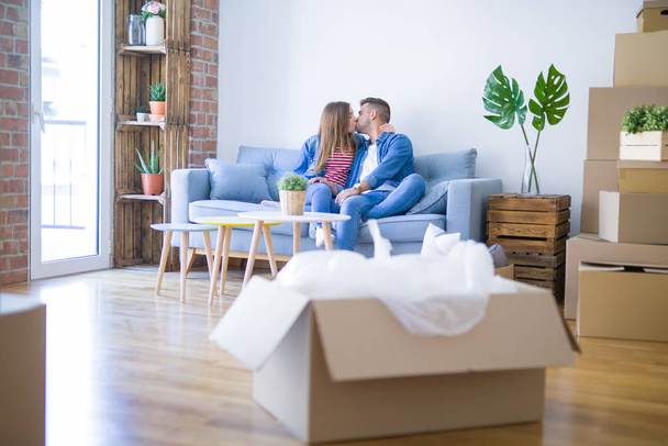 Young beautiful couple sitting and hugging on the sofa at new apartment with cardboard boxes around them, very excited for moving to a new home - Photo, image