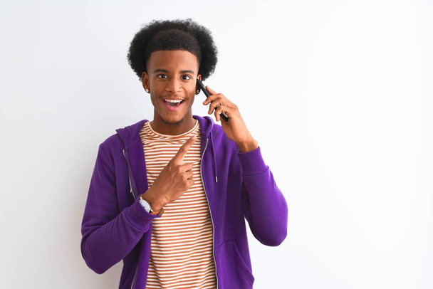Young african american man talking on smartphone standing over isolated white background very happy pointing with hand and finger - 写真・画像